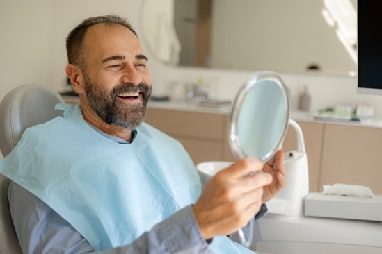 A man smiles to look at his new dental crowns from Twin Aspen Dental Center in Parker, CO.